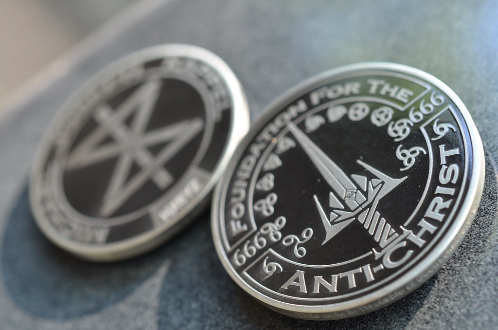 Two custom metal Ghrisx coins photographed on a tabletop, one showing the personal symbol and one showing an engraved sword-like emblem.